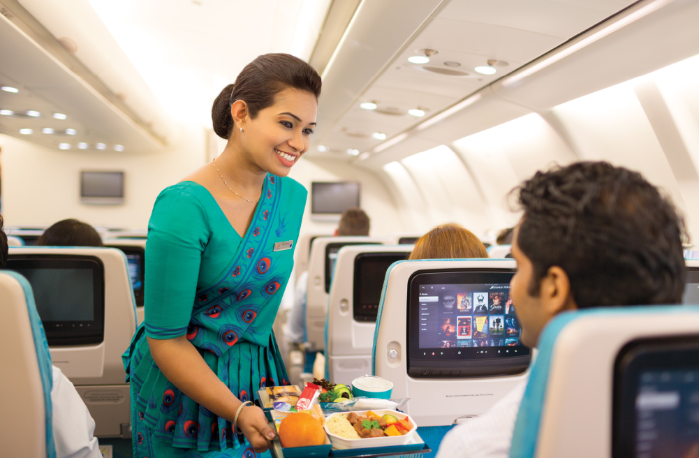 An air hostess serves food to a smiling female passenger